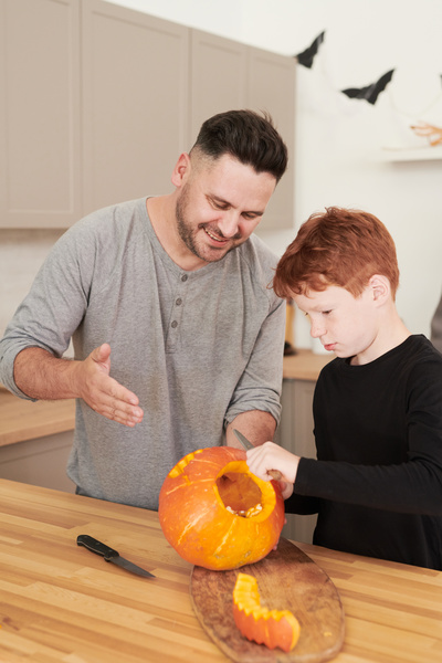 Man Helps His Son Carve Muzzle on Pumpkin